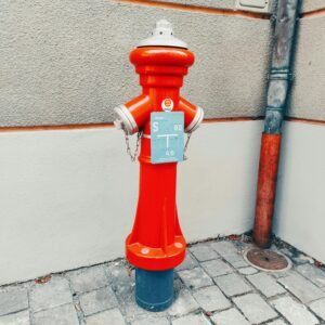 A vibrant red fire hydrant stands along a cobblestone sidewalk in Amberg, Germany, highlighting urban safety.